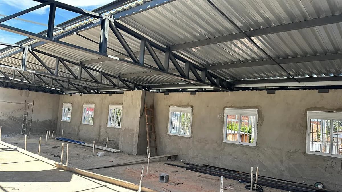 Interior de obra com estrutura metálica de cobertura e alvenaria em execução